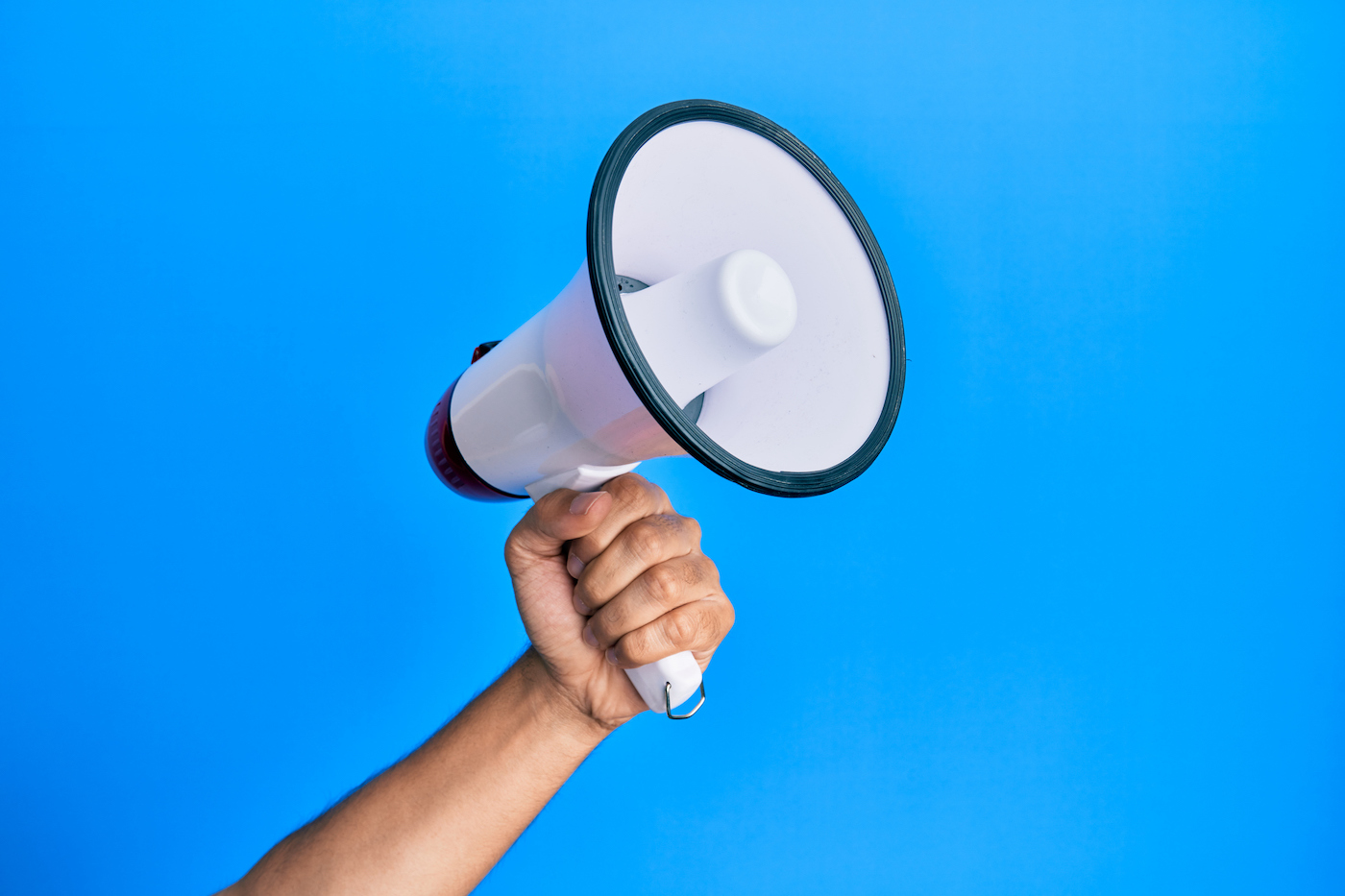 Hand of hispanic man holding megaphone over isolated blue background.