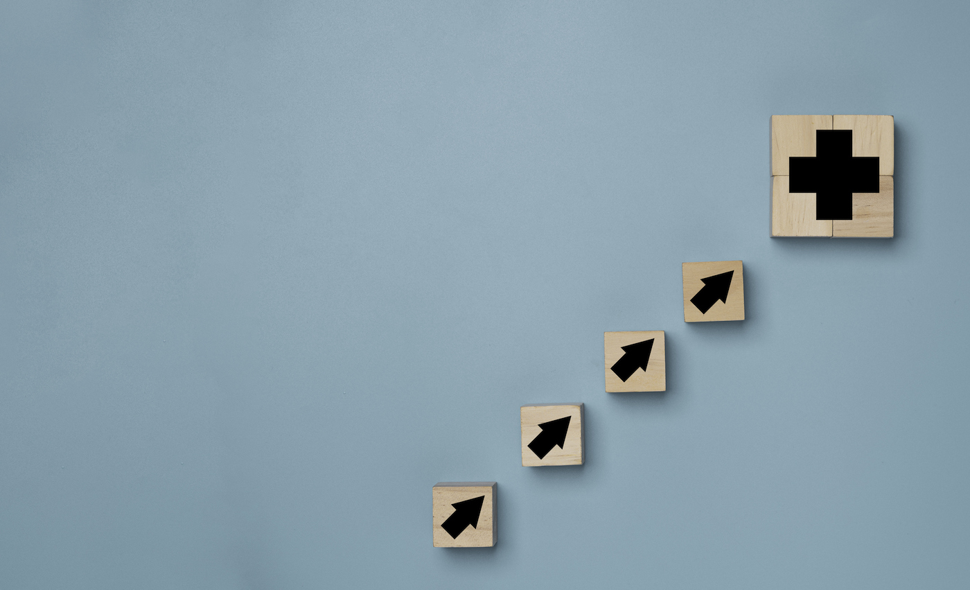 Plus sign and increasing arrow print screen on wooden cube block on blue background which it mean positive sign such as more benefit thinking and mindset concept. (Plus sign and increasing arrow print screen on wooden cube block on blue background whi