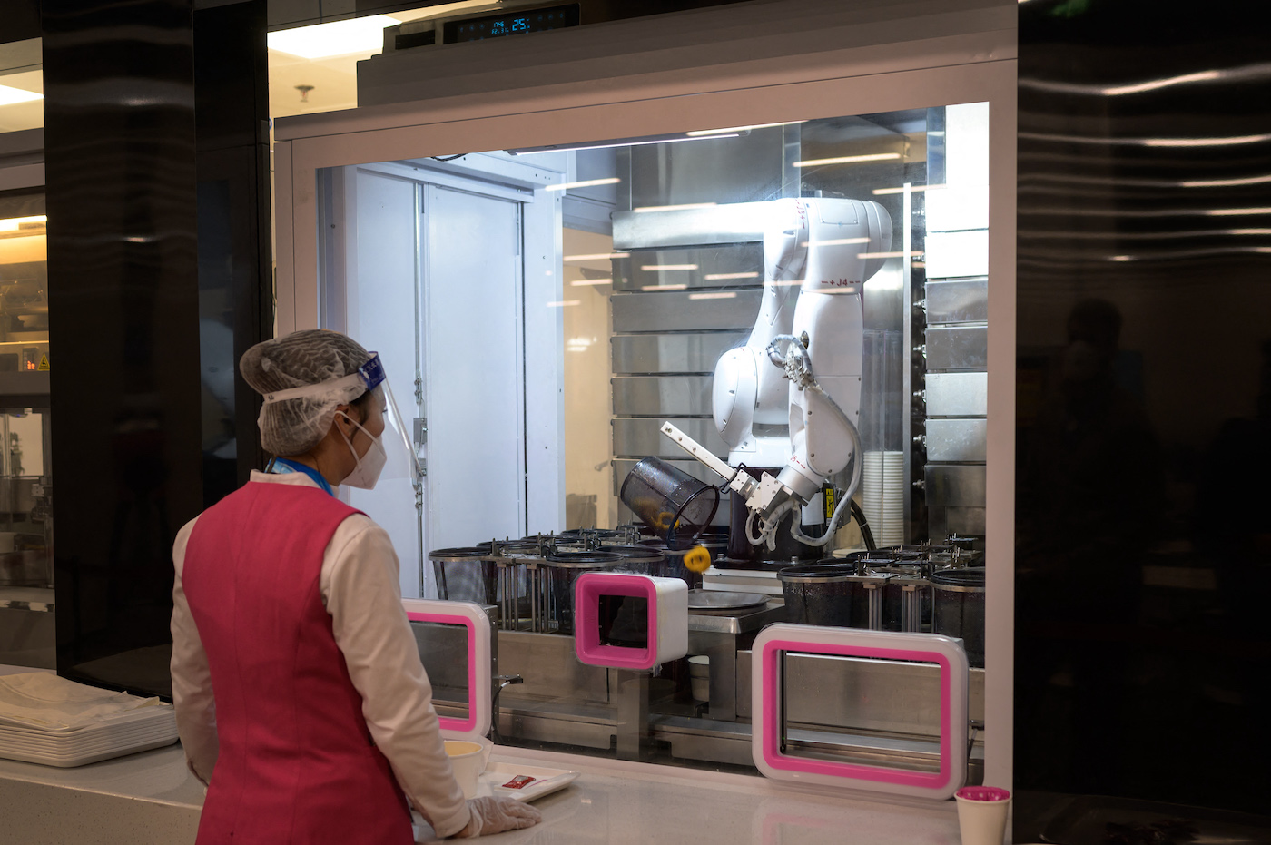 A worker waits for a robot processing an order at the dining hall of the Main Press Center ahead of the 2022 Winter Olympics in Beijing, on January 28, 2022. (Photo by Fabrice COFFRINI / AFP) (Photo by FABRICE COFFRINI/AFP via Getty Images)