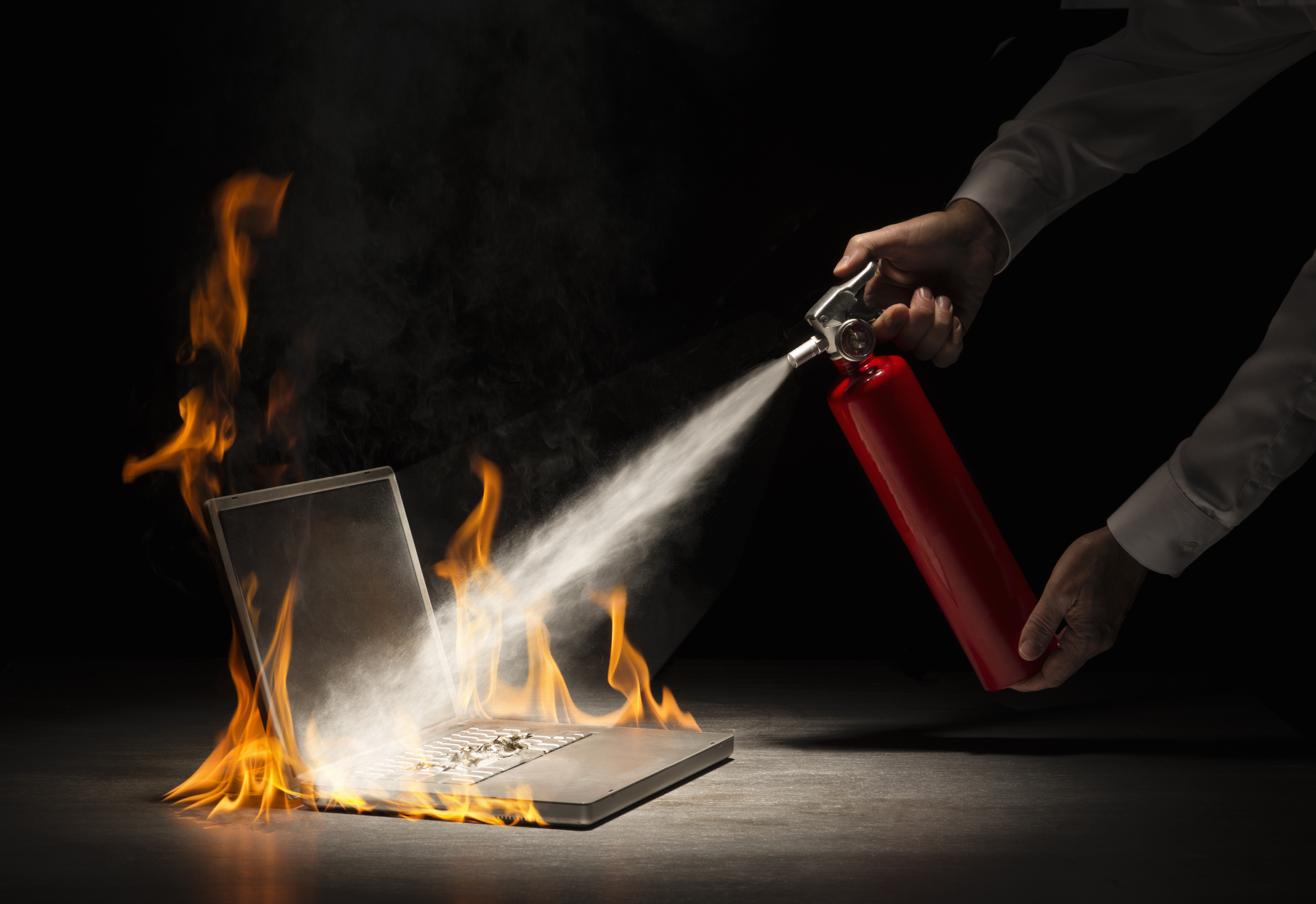 Businessman using fire extinguisher on laptop computer that is in flames