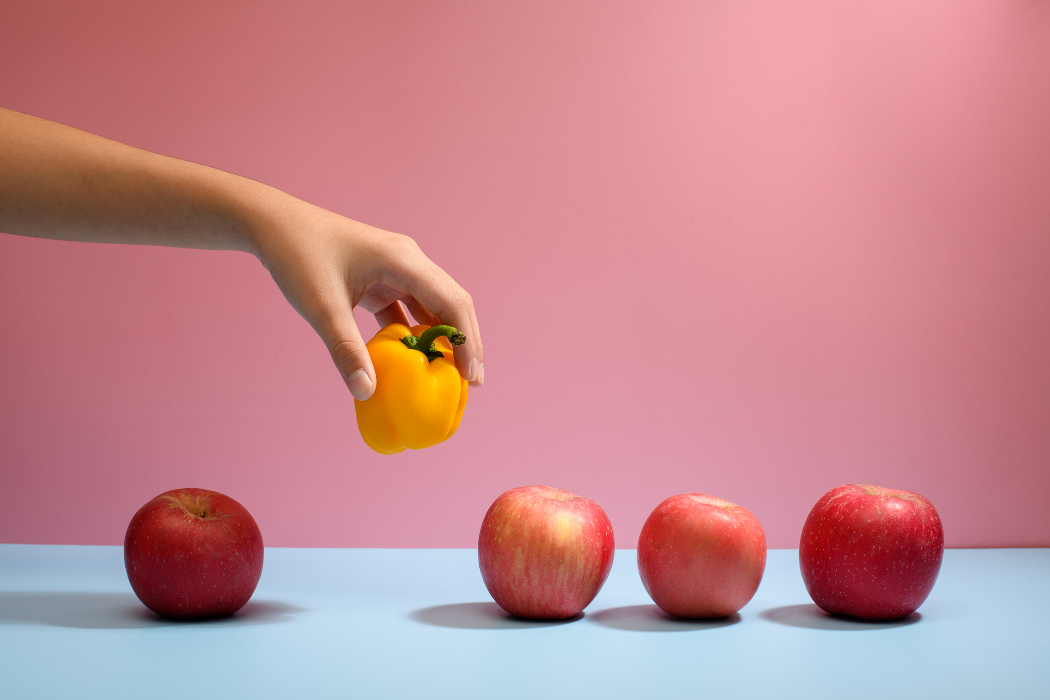 Hand picking a yellow bell pepper standing out from apples
