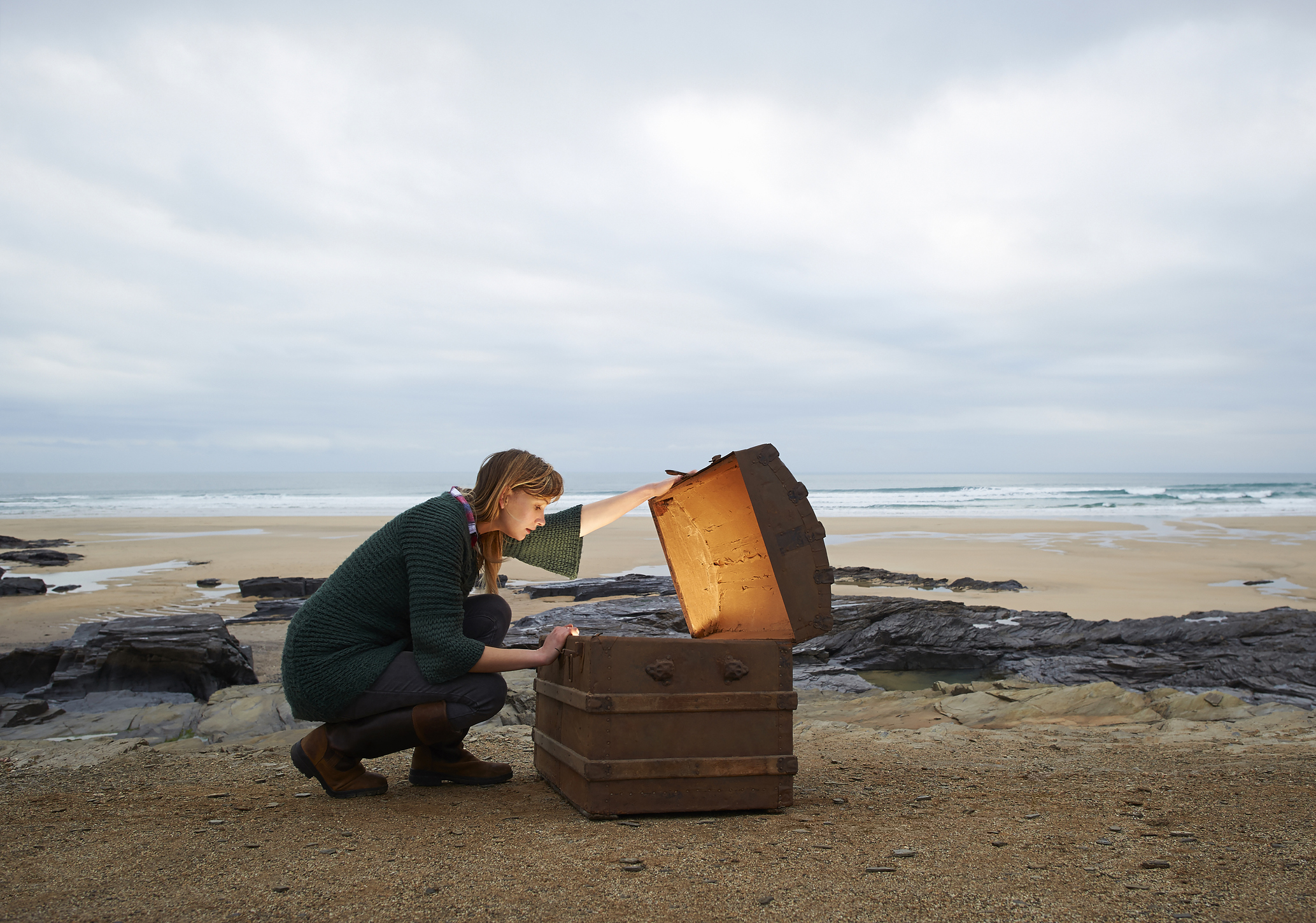 Woman looking inside treasure chest on deserted beach.