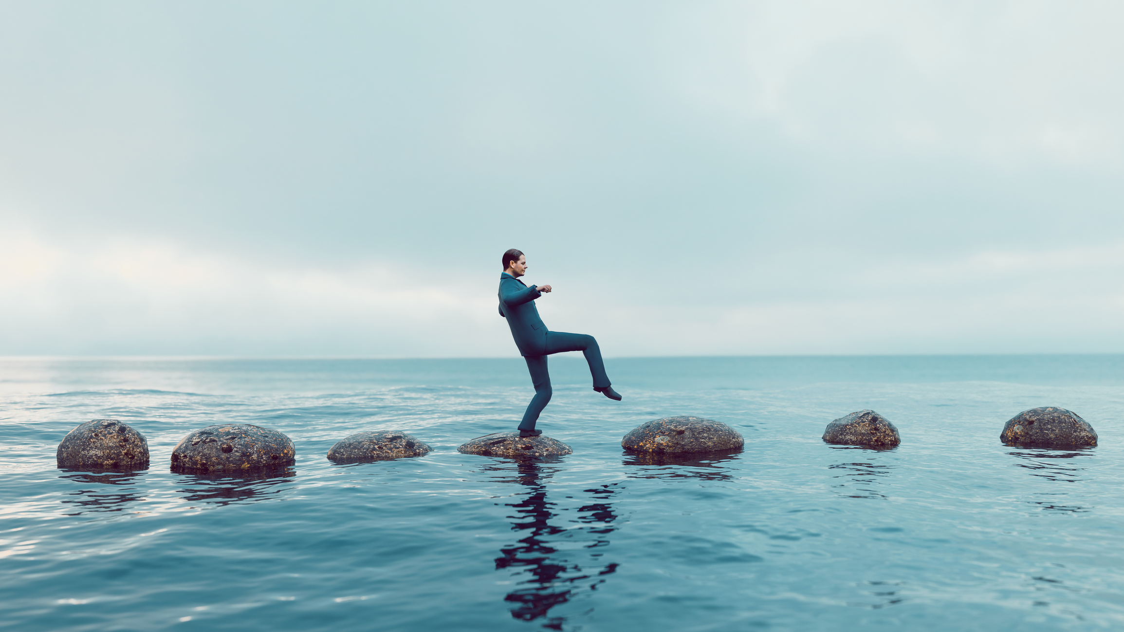 Man walks carefully on a path of small rocks in the middle of the sea; private equity must deal carefully with sanctions