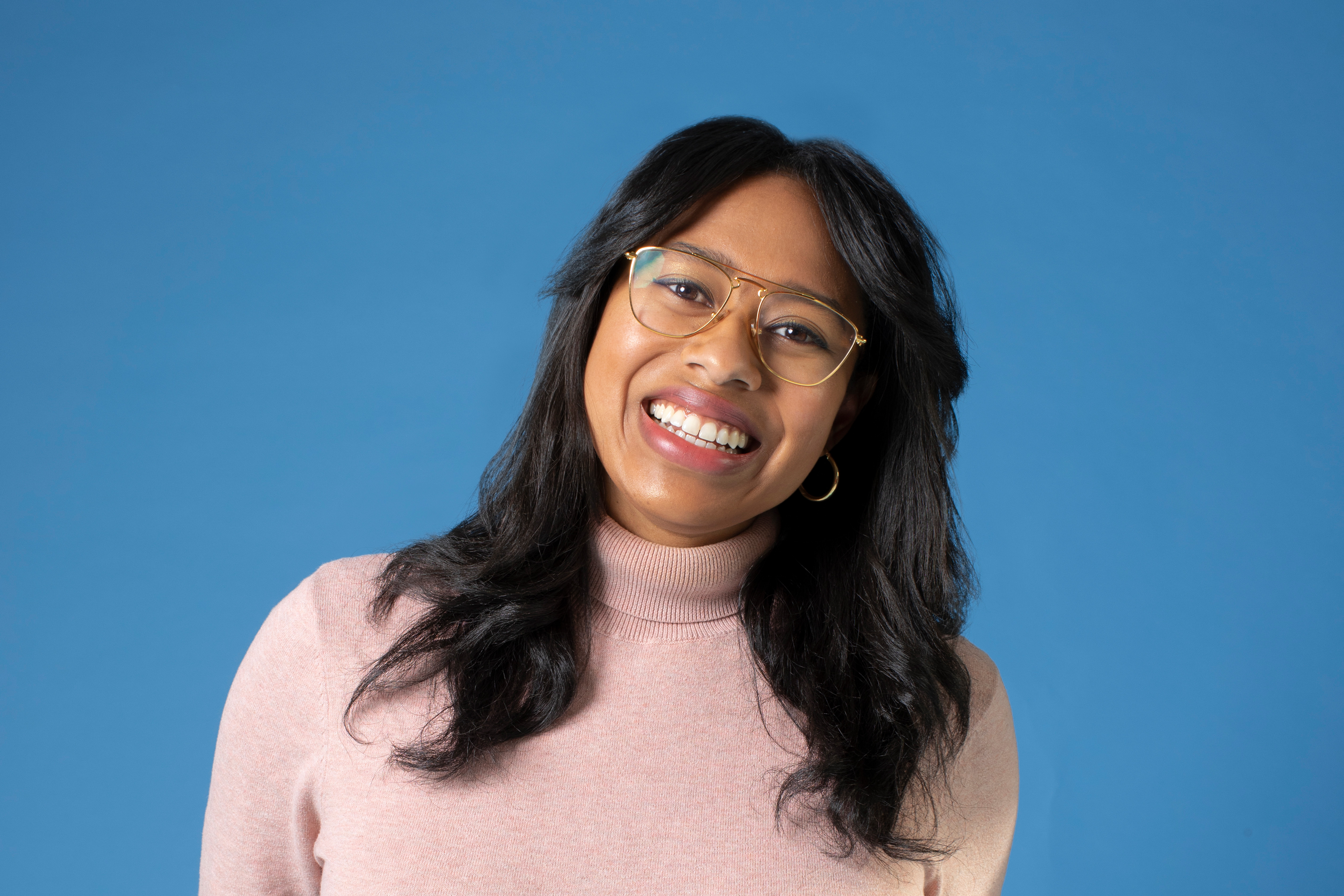 Pilar Johnson smiles to camera wearing glasses and pink turtleneck