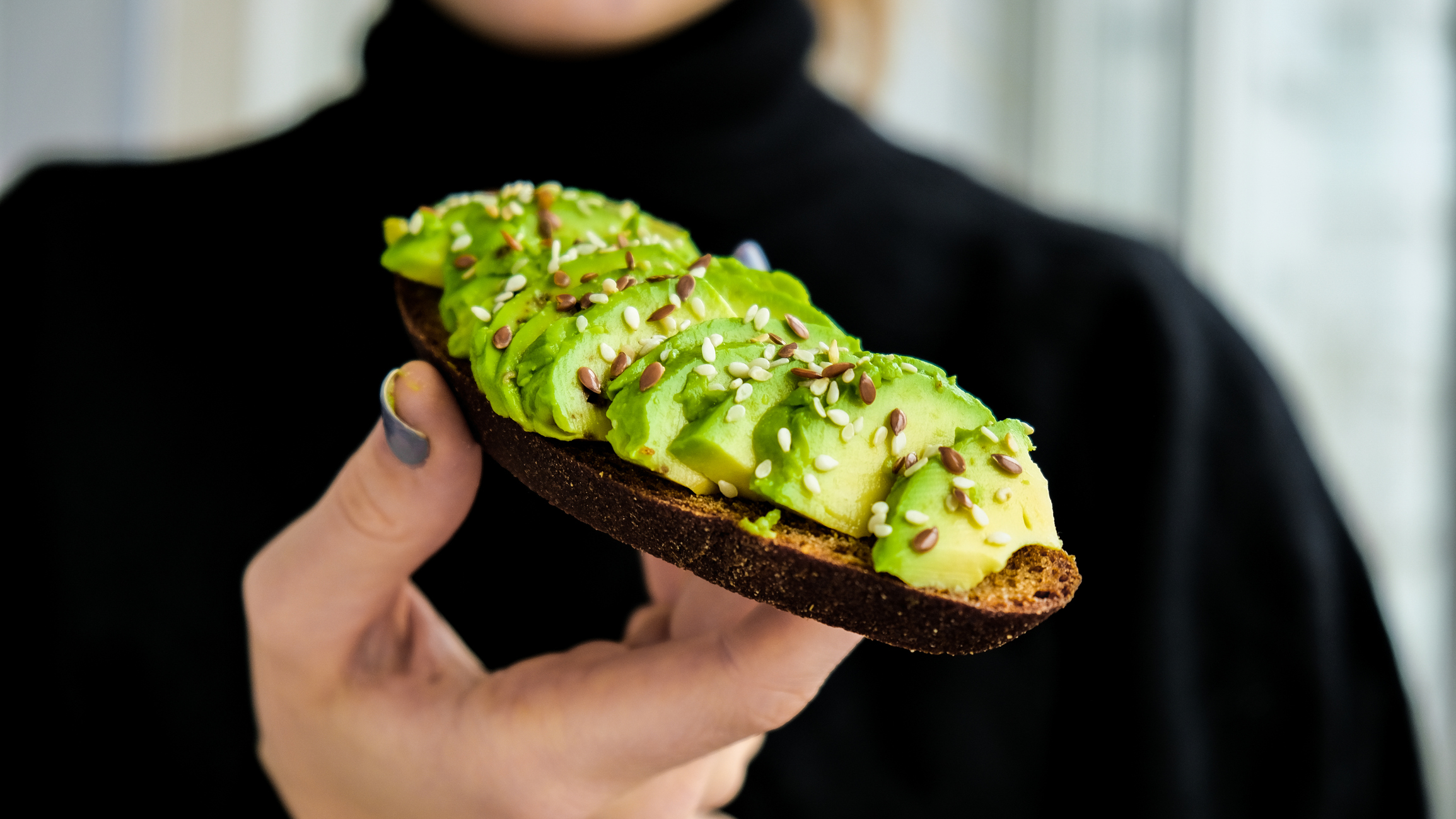 Hand Holding Avocado Toast. Ripe Hass Avocado, Wholegrain Bread, Sesame Flax Seeds.